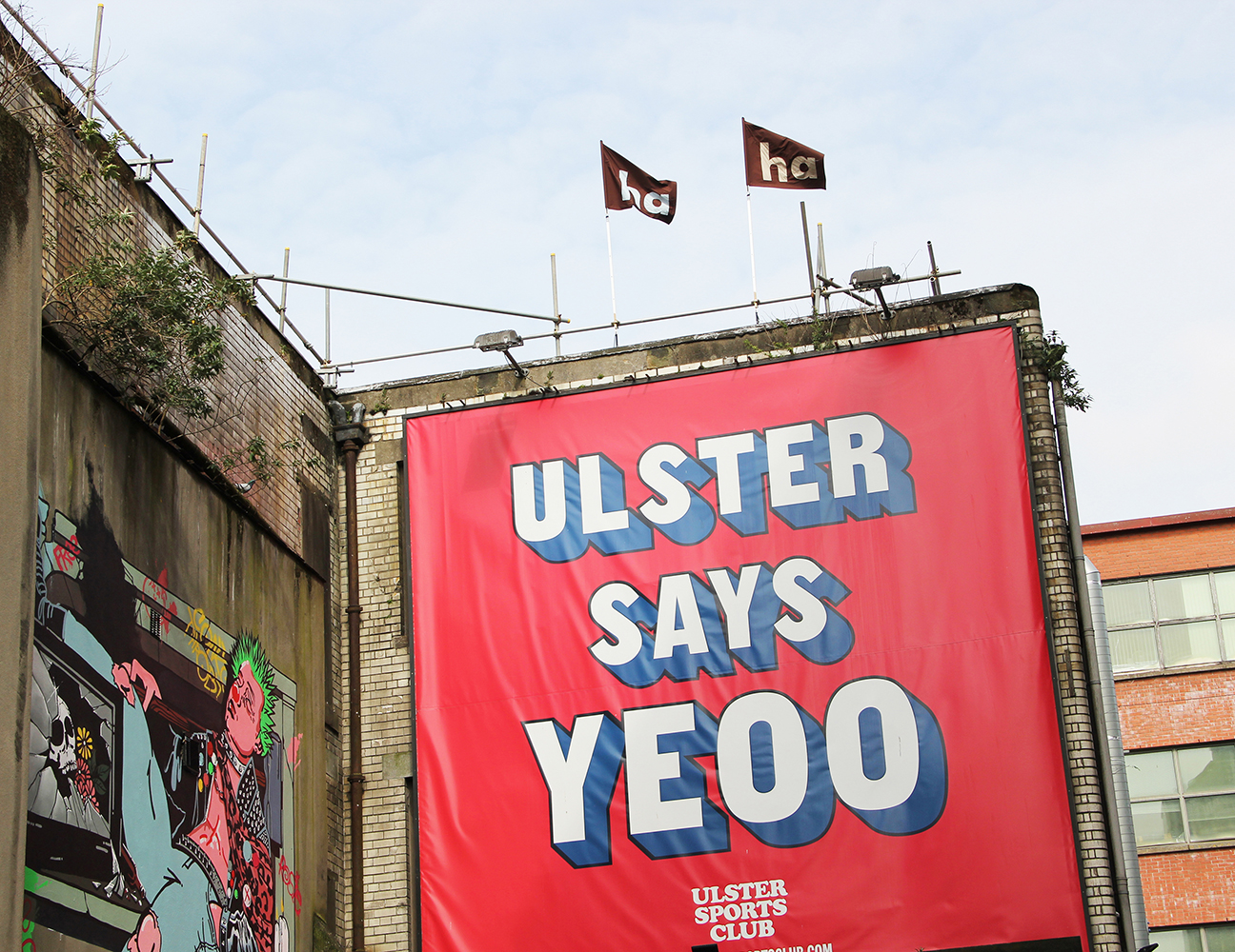 Image of two 'ha ha' flags on the roof above the Ulster Sports Club Bar - above a billboard saying "Ulster Says Yeoo".